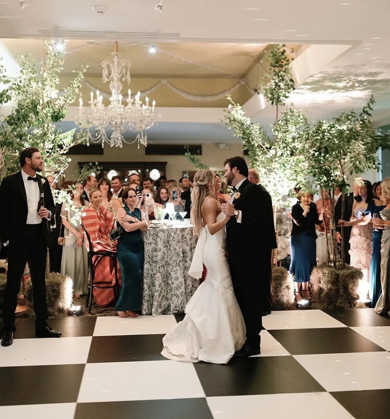 Checkered dance floor surrounded by greenery and floral installations at an indoor Los Angeles wedding reception